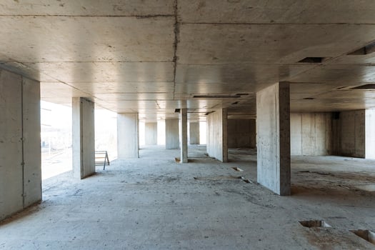 A large, spacious empty room featuring unfinished concrete walls and sturdy pillars, all situated within a building that is currently under construction and is not yet complete photo