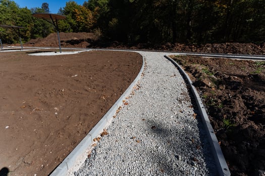 A lovely and charming gravel path winds its way through a vast and expansive dirt field, with magnificent towering trees in the background, creating a truly picturesque natural scene photo