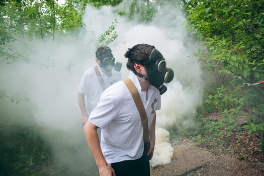 Two men wearing gas masks walking through a forest photo