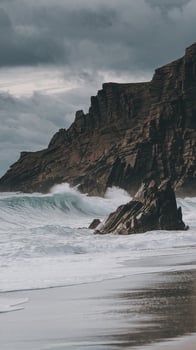 Dramatic Ocean Waves Crashing on Rocky Cliffside with Moody Sky and Sandy Shoreline photo