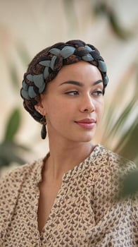 Woman with braided headscarf and patterned blouse in a soft natural setting with green leaves photo