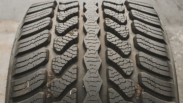 Closeup of black car tire tread with intricate geometric patterns on concrete surface background photo