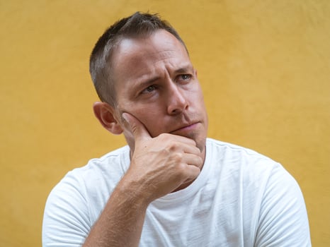 Thoughtful Man Wearing White Shirt Thinking Against Yellow Wall Background Outdoors in Daylight photo
