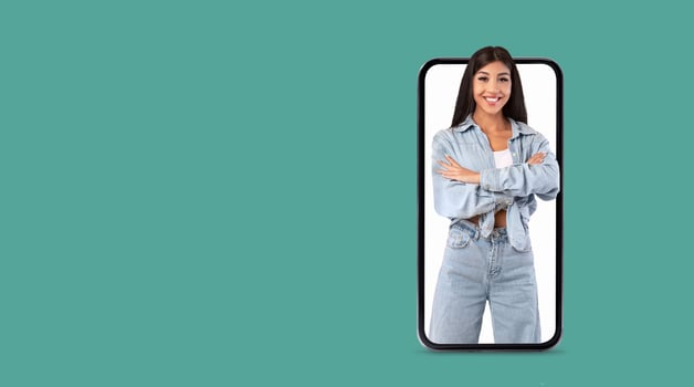 A young woman confidently poses with arms crossed, showcasing her cheerful demeanor on a large smartphone screen. The background is a solid color, emphasizing her presence and the technology. photo