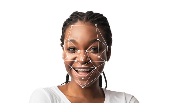 A person with braided hair smiles confidently while technology overlays a facial recognition grid on their face. This illustrates advancements in identification and facial data analysis. photo