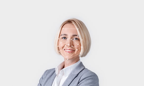 A person with short blonde hair is smiling confidently in a professional outfit. A digital overlay of facial recognition technology is displayed, indicating identification efforts. photo
