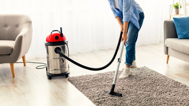 Household And Cleaning Concept. Smiling casual lady using vacuum cleaner on rug floor carpet, listening to music, wearing wireless headset, free copy space. Millennial woman enjoying everyday routine photo
