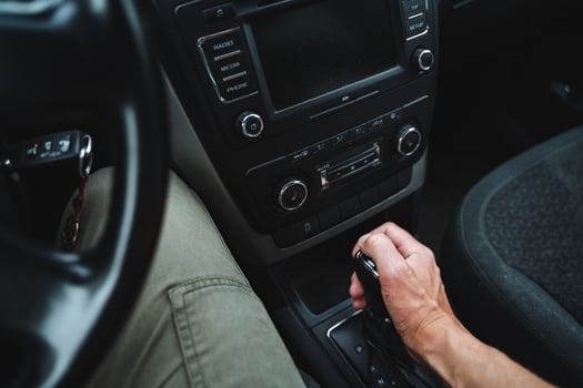 The person in the car is manually changing gears while driving by operating the gear shifter. This process takes place inside the vehicle, requiring the drivers attention and skill photo