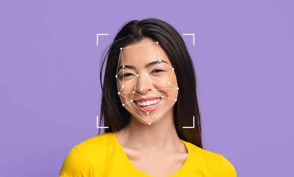 A woman with long, dark hair smiles while facial recognition technology maps her face. The background is a solid purple, emphasizing the facial identification process and her expression. photo