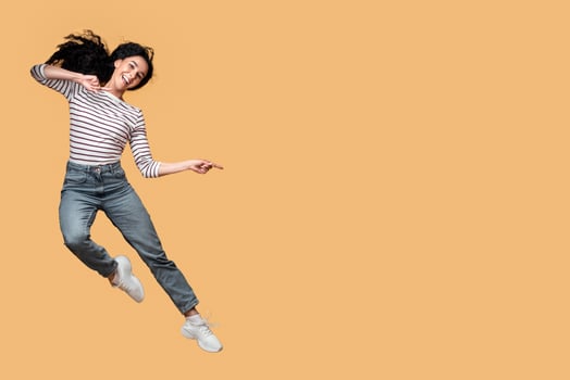Great Promo. Carefree Young Arab Couple Jumping And Pointing In The Middle, Excited Happy Middle Eastern Man And Woman Demonstrating Copy Space For Your Design On Yellow Background, Full Length photo