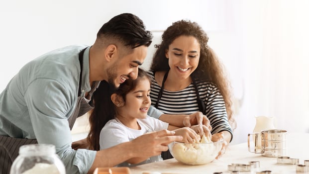Cheerful father, mother and daughter middle-eastern family baking at kitchen, wearing aprons and making dough for cookies. Loving mom, dad and kid spending time together at home, copy space photo