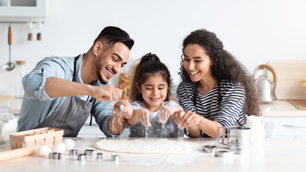 Cheerful arab father, mother and daughter making biscuits together, rolling pastry dough and adding flour, middle-eastern mom and dad showing their little kid how to make cookies, kitchen interior photo