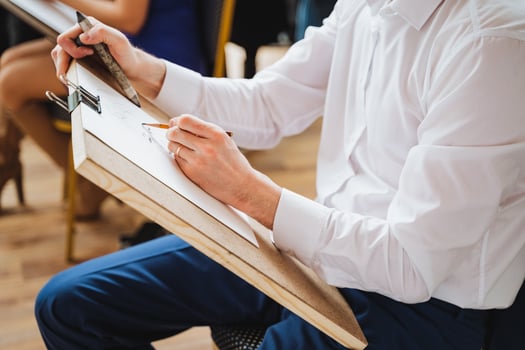 A man sits at a hardwood desk drawing on paper with a sleeve and thumb gesture photo
