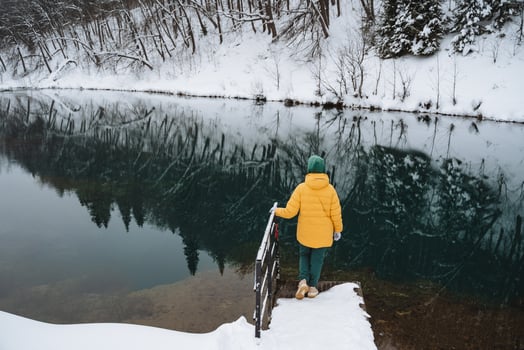 A person wearing a bright yellow jacket is standing on a wooden dock while looking out over a serene lake, enjoying the peaceful view of the water and surrounding nature photo