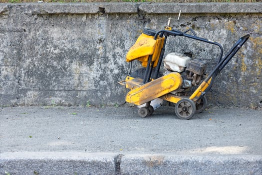 An old worn-out gasoline cutter stands against a concrete wall. photo