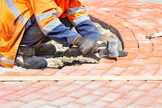 A squatting worker lays paving slabs by a wooden level on a sunny summer day. photo