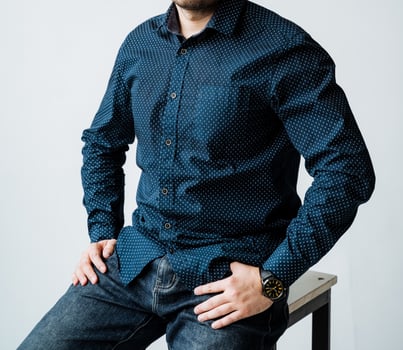 A man who is wearing a stylish blue shirt is comfortably sitting on a stool with his hands confidently placed on his hips, appearing relaxed and at ease in his surroundings photo