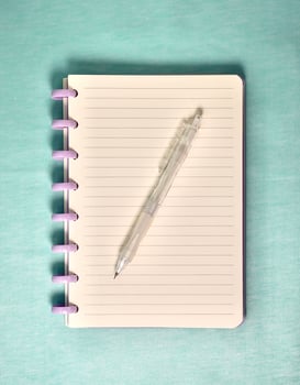 Note book with white lined paper and purple spiral spine and mechanical pencil above the paper isolated on vertical light blue background. photo