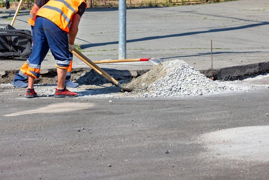 Construction worker repairs a road with gravel and tools in bright sunlight. Copy space. photo