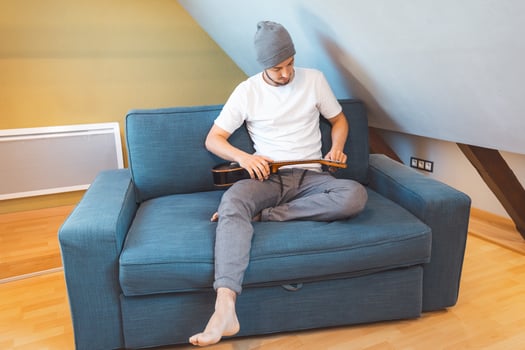Male with beanie plays ukulele on a sofa in natural light photo