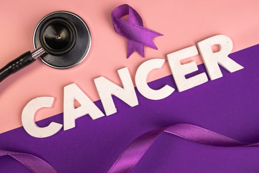 A stethoscope and purple ribbons are arranged near the word CANCER. World cancer day concept photo