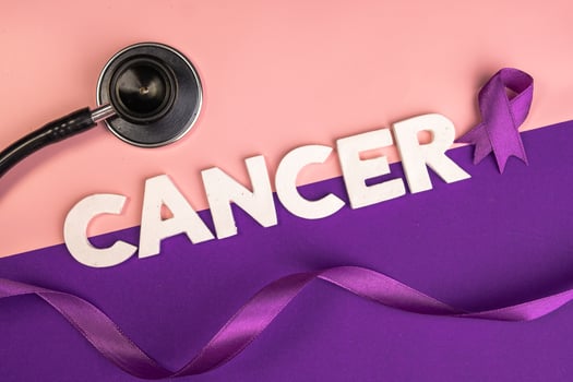 A stethoscope lies near the word CANCER spelled out in white letters and a purple ribbon. International cancer day concept photo