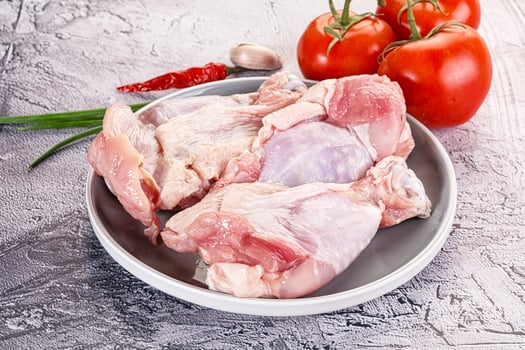 Raw chicken legs on a plate with tomatoes and garlic photo