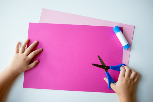 Childs hands crafting with pink paper, blue scissors, and glue on light background photo