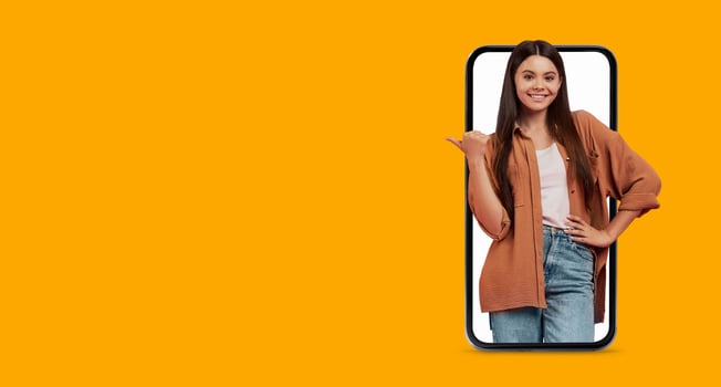 A woman stands confidently, smiling and pointing to her smartphone with a large screen. The bright background enhances the technology and communication aspects of the scene. photo