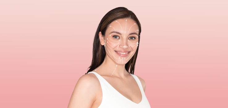 A woman engages in a self-care skincare routine, smiling and relaxed. She stands against a soft pink background, showcasing her commitment to beauty and wellness. photo