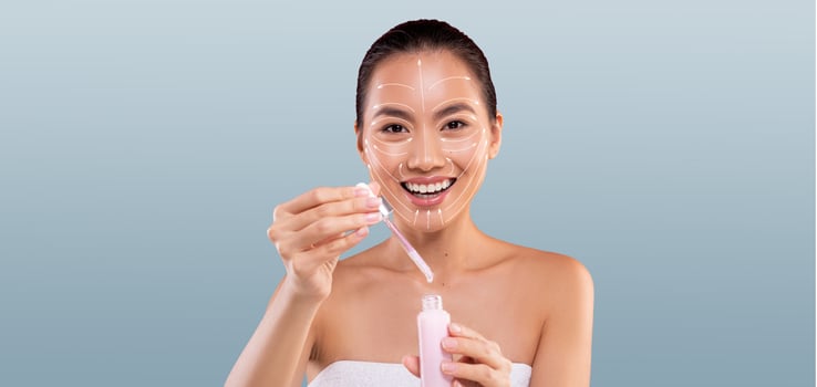 Asian woman is happily applying a skin care product to her face, radiating joy and satisfaction. She is isolated against a soft background, perfect for a pampering beauty routine. photo