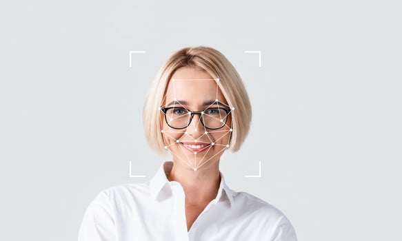 A person with short blonde hair wears glasses while smiling confidently. The focus is on facial recognition technology, highlighting features and characteristics in a neutral setting. photo