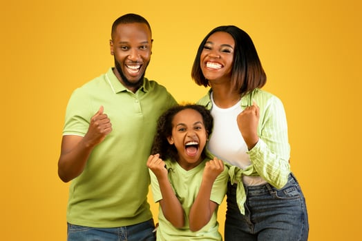 Victory concept. Emotional overjoyed black family of three shaking fists, gesturing yes and shouting, standing over yellow background. Young parents and daughter rejoicing success. photo