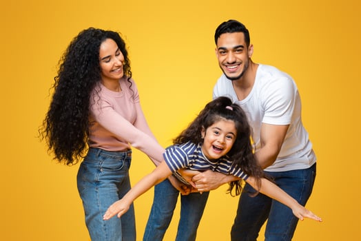 Family Fun. Portrait Of Cheerful Arab Parents Playing With Their Little Daughter, Funny Female Child Pretending Flying, Spreading Hands, Fooling Together With Mom And Dad Over Yellow Background photo