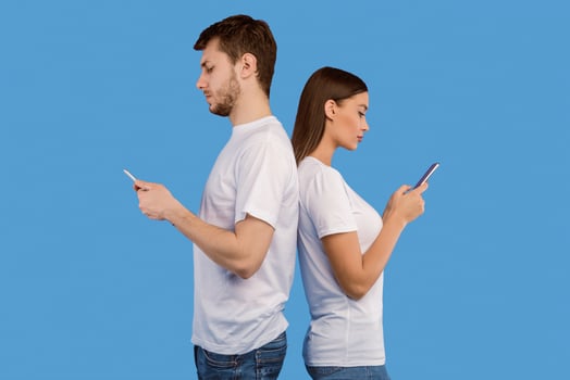 Smartphone Addiction. Serious man and woman standing back to back and using their smart phones, purple studio wall photo