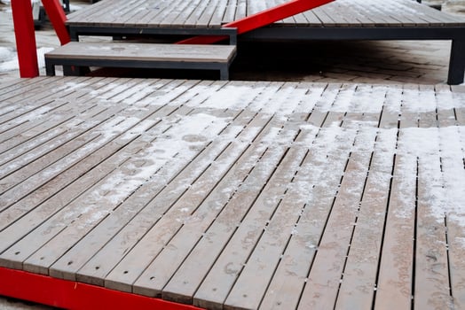 A stunning wooden deck, adorned with soft snow, features a vibrant red railing that contrasts beautifully with the pristine white snow, creating a picturesque winter scene photo
