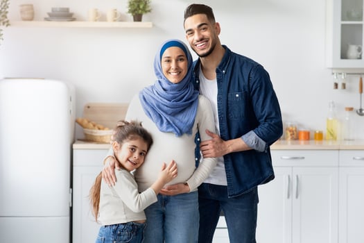Islamic Expecting Family. Happy Pregant Muslim Woman In Hijab Posing With Husband And Little Daughter, Arab Spouses And Cute Female Child Standing In Kitchen Interior And Smiling At Camera photo