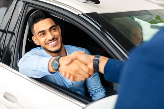 Cheerful arabic man sitting in new white car, shaking unrecognizable auto showroom sales assistant hand, celebrating successful deal. Handsome wealthy middle-eastern guy buying automobile, closeup photo