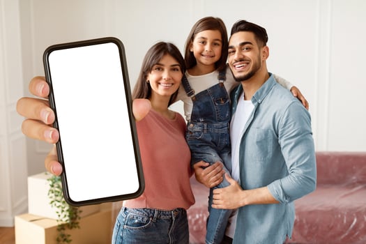 Portrait Of Happy Young Family Showing Key, Cheerful Parents Hugging Little Kid, Holding Daughter On Hands. Smiling People Moving In New Apartment Standing In Living Room. Selective Focus photo