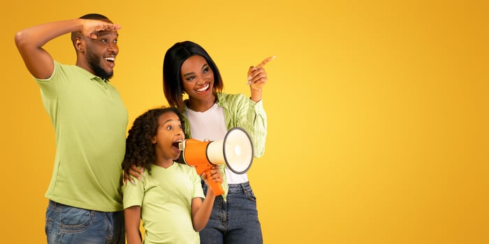 Happy african american family of three making announcement, girl talking at loudspeaker and looking together at copy space on yellow background, panorama, studio shot photo