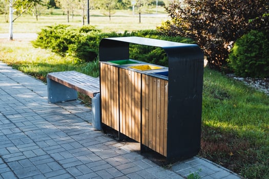 In a lovely park, a wooden trash can is placed conveniently next to a sturdy bench, providing a neat solution for waste disposal while enjoying the greenery and fresh air around photo