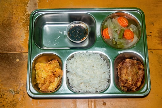 A nutritious and balanced free lunch featuring rice, fried chicken, vegetable soup, and a dipping sauce, served in a stainless steel tray on a rustic wooden table photo