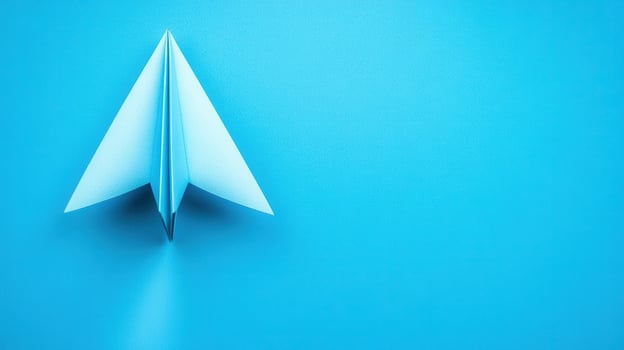 Creative paper airplane takes flight on a vibrant blue surface in a minimalistic setting during daylight photo