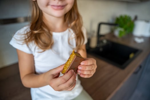 Little girl eating Dubai chocolate with pistachio paste and kataifi dough. Confectionery handmade sweets at home in the kitchen. High quality photo