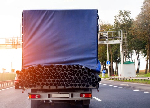 A tilt van transports an oversized cargo of metal pipes along the road against the backdrop of a sunset, close-up photo