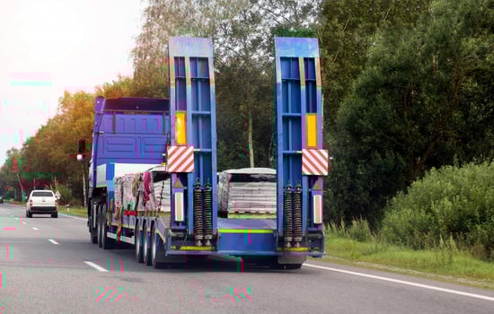 A modern truck with a low-loader transports paving slabs along a highway in the summer. Trawl trailer services and rental photo
