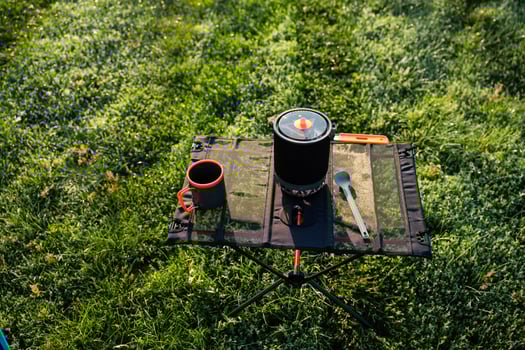 A convenient and portable camping cooking setup featuring pot and utensils resting on lush green grass photo