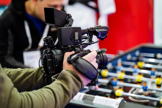 A man is standing and holding a camera in front of a foosball table, which is a popular arcade game that involves players manipulating rods to kick a ball into the opposing goal photo