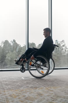 A businessman in a wheelchair enjoys a moment of laughter by a large window in a modern office, embodying positivity, resilience, and a balanced approach to work and life. photo