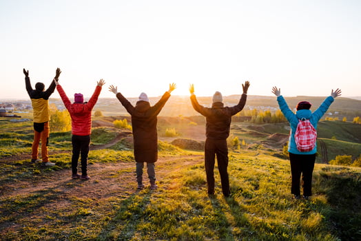 Group of people on hilltop, arms in air, enjoying natural landscape and blue sky photo